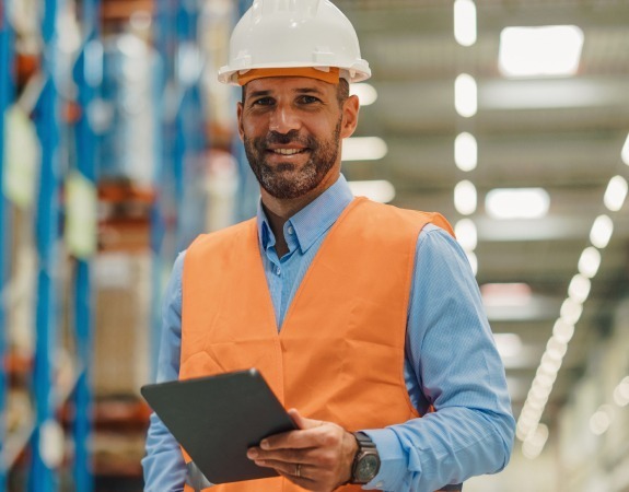 Man in warehouse wearing orange high-visibility vest and hard hat