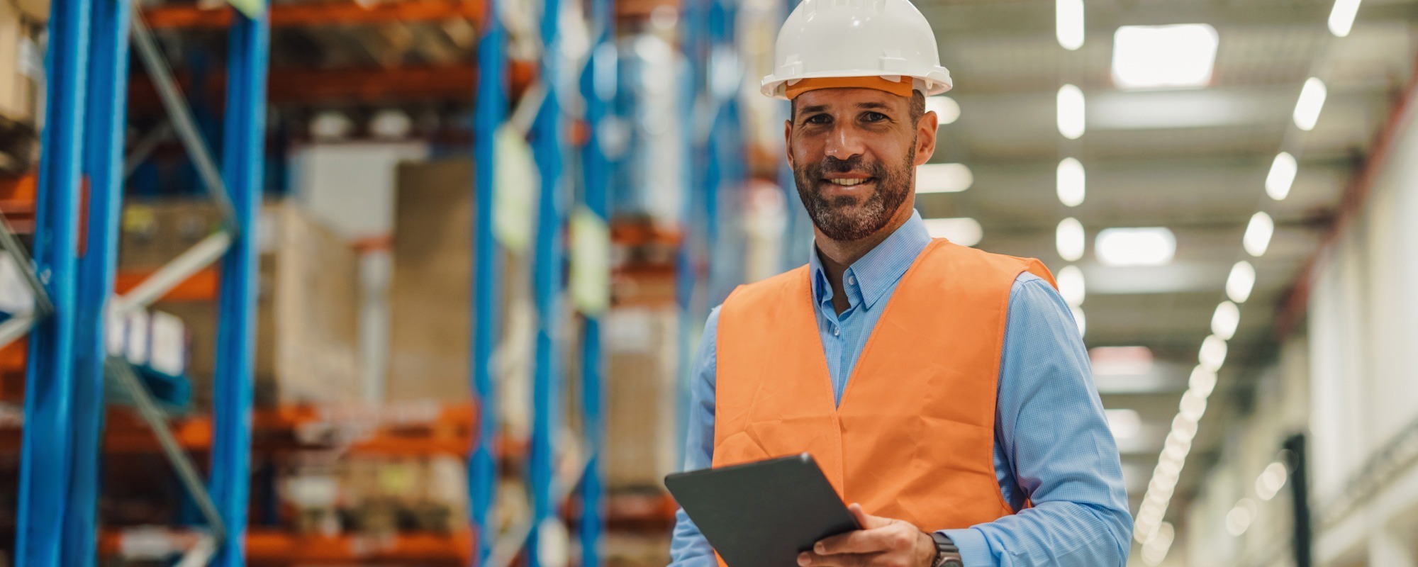 Man in warehouse wearing orange high-visibility vest and hard hat