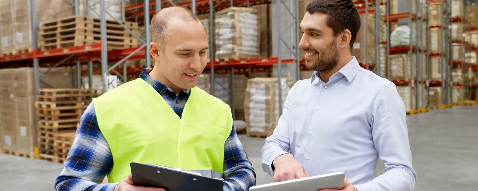 Warehouse worker in high-vis and supervisor in shirt collaborating in front of racking