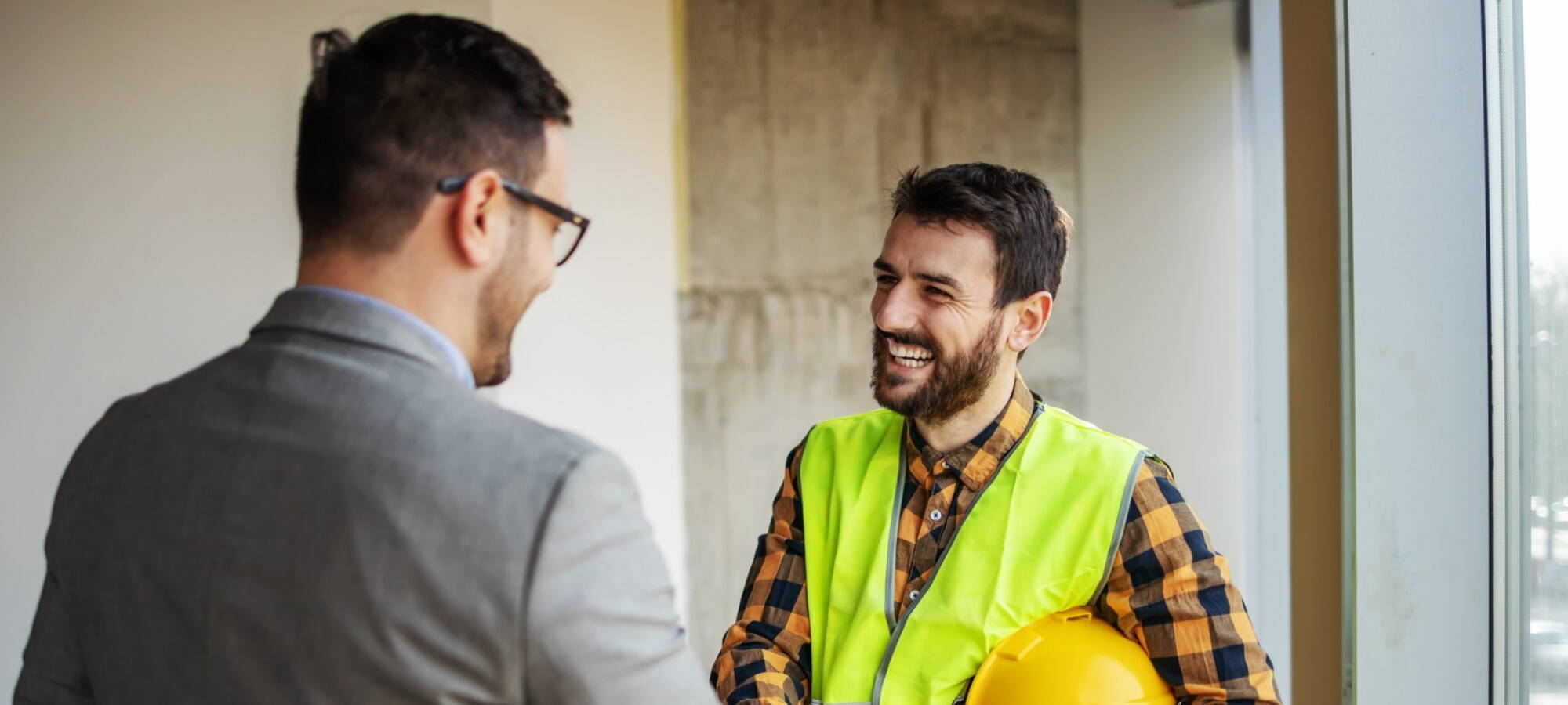 Man in high-visibility vest and man in suit shaking hands, representing successful recruitment partnership